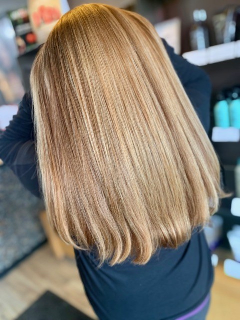 Salon Indigo in Fraser, MI Person with straight, shoulder-length, light brown hair facing away from the camera in an Aveda Salon setting. Salon Indigo in Fraser, MI