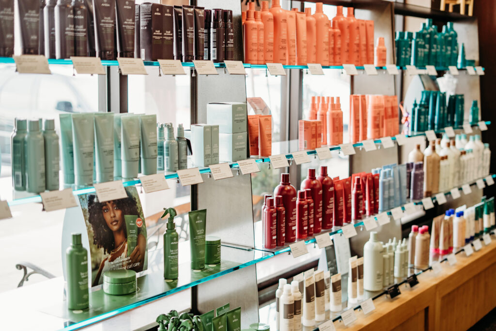 Salon Indigo in Fraser, MI Shelves display various hair care products and skin care items in colorful bottles and tubes, organized by brand and type, in a well-lit store or salon setting. Salon Indigo in Fraser, MI