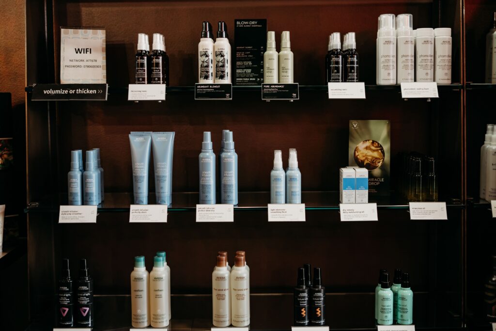 Salon Indigo in Fraser, MI Shelves display various hair care products, including shampoos, conditioners, sprays, hair color, and serums, arranged in rows with labels and informational signs. Salon Indigo in Fraser, MI