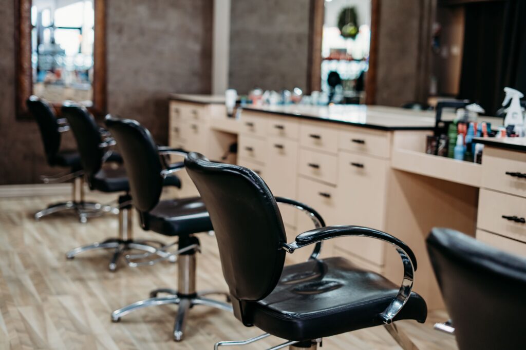 Salon Indigo in Fraser, MI Row of empty black salon chairs facing a counter with mirrors and various hair styling products, including options for hair color, in a modern hair salon. Salon Indigo in Fraser, MI