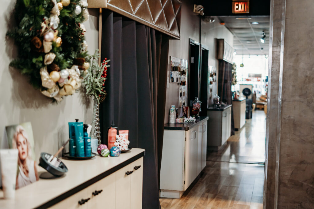 Salon Indigo in Fraser, MI A hallway in an Aveda Salon with hair products, a holiday wreath on the wall, styling stations along the corridor, and areas for manicure pedicure and skin care services. Salon Indigo in Fraser, MI